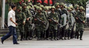 An ethnic Uighur man walks in front of armed Chinese paramilitary police in riot gear as they patrol a main street in Urumqi