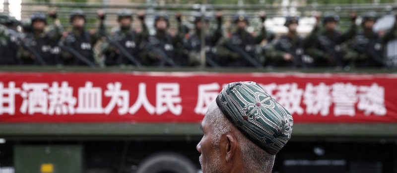 A Uighur man looks on as a truck carrying paramilitary policemen travel along a street during an anti-terrorism oath-taking rally in Urumqi